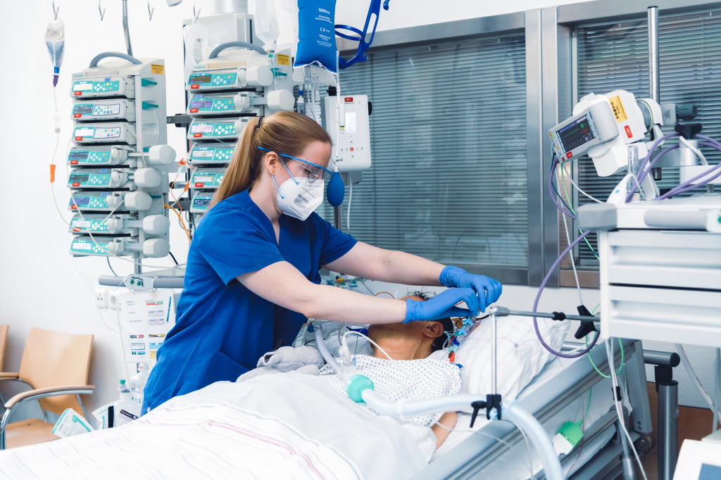 Weibliche Pflegefachkraft versorgt einen intubierten Patienten in seinem Bett auf der Intensivstation
